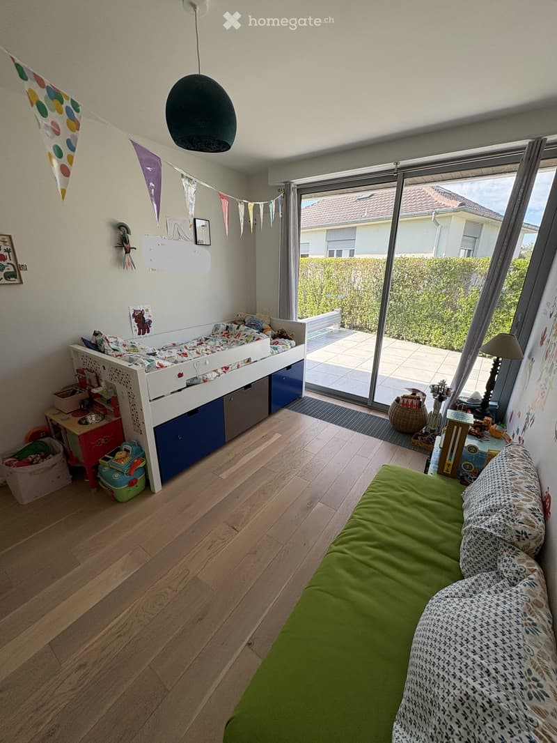 Bright, modern children's bedroom with wooden flooring, a green sofa, a white loft bed with storage, a small table, and various toys and decorations.