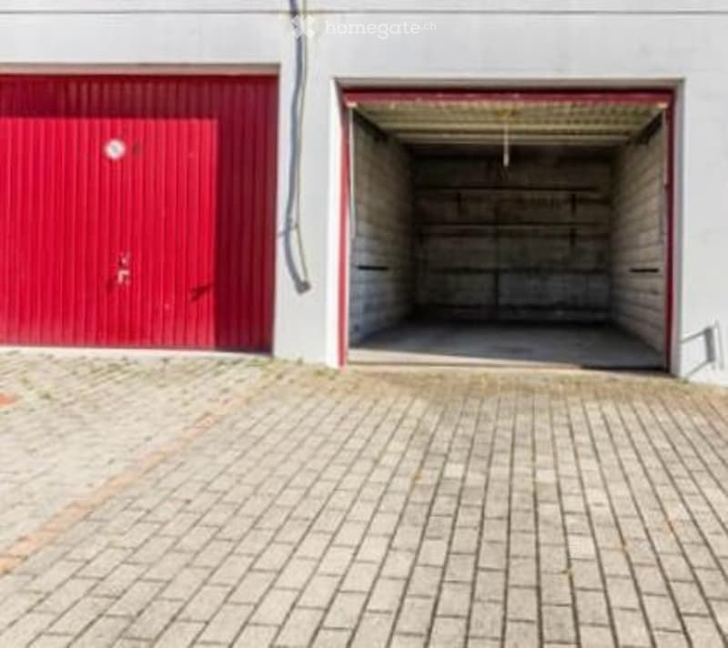 A building exterior featuring a large red garage door and an open garage space with concrete walls and a concrete floor.