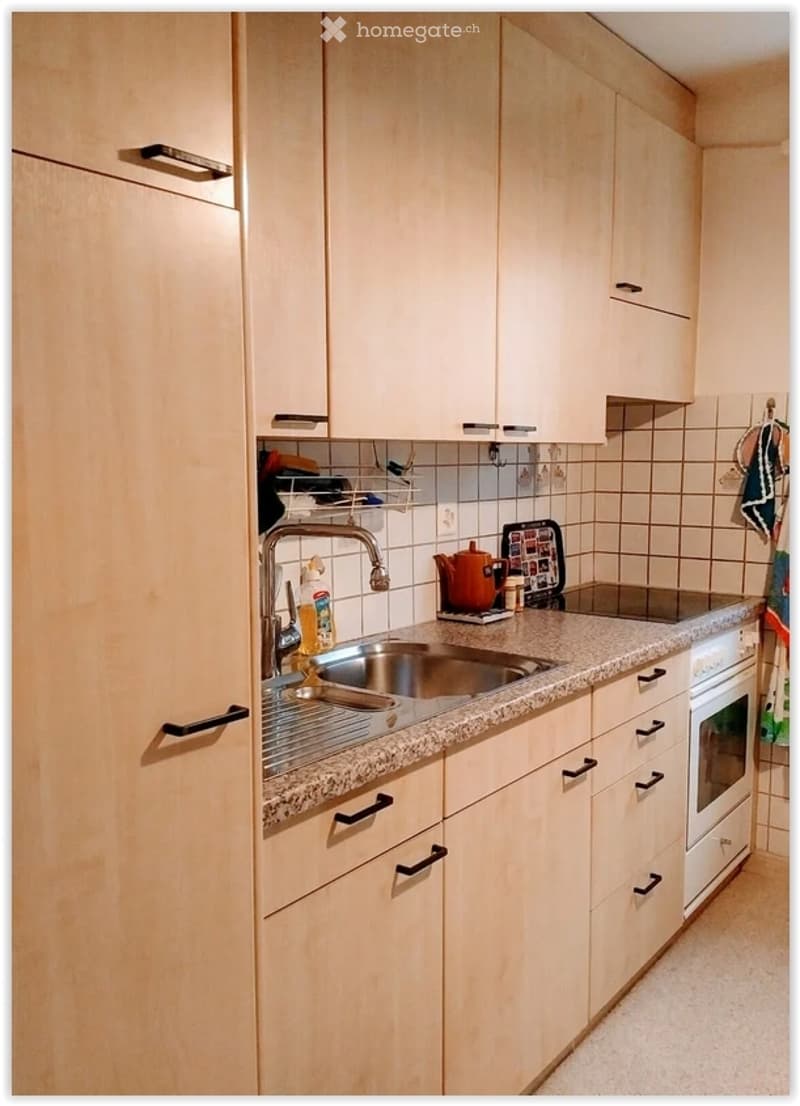 Modern kitchen with light wood cabinets, granite countertop, stainless steel sink, and various appliances.
