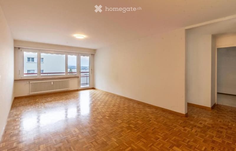 Empty room with wooden flooring, large windows, radiator, and access to a balcony.