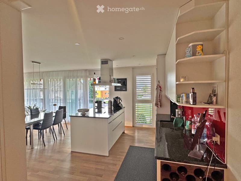 open kitchen with dining area, center island, wooden floor, white cabinets, black countertops, built-in shelves, kitchen appliances, dining table and chairs, large windows with curtains