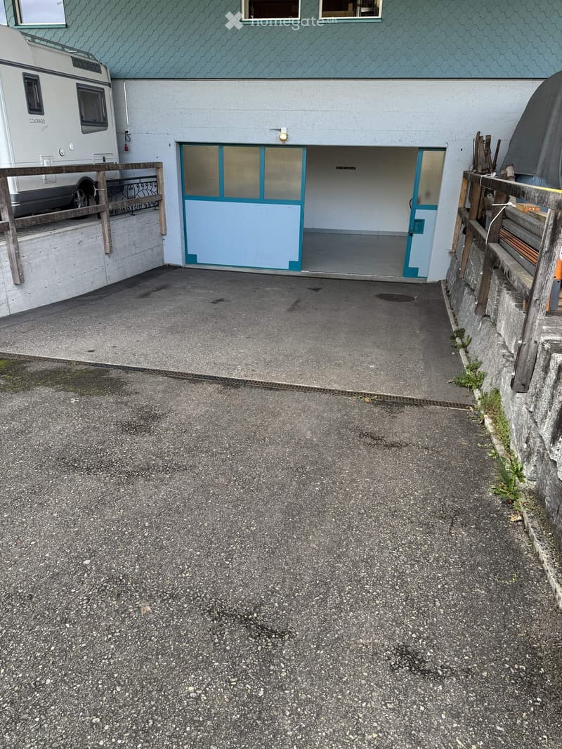 Garage with two doors, concrete floor, wall with windows, parked camper van