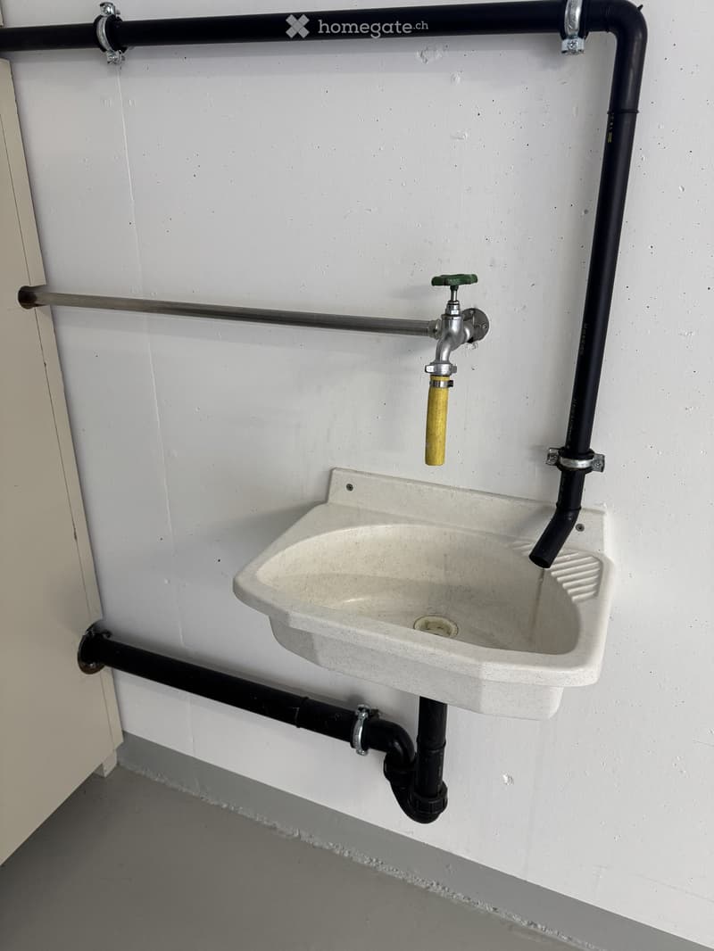 A white sink mounted on a white wall with a faucet and pipes