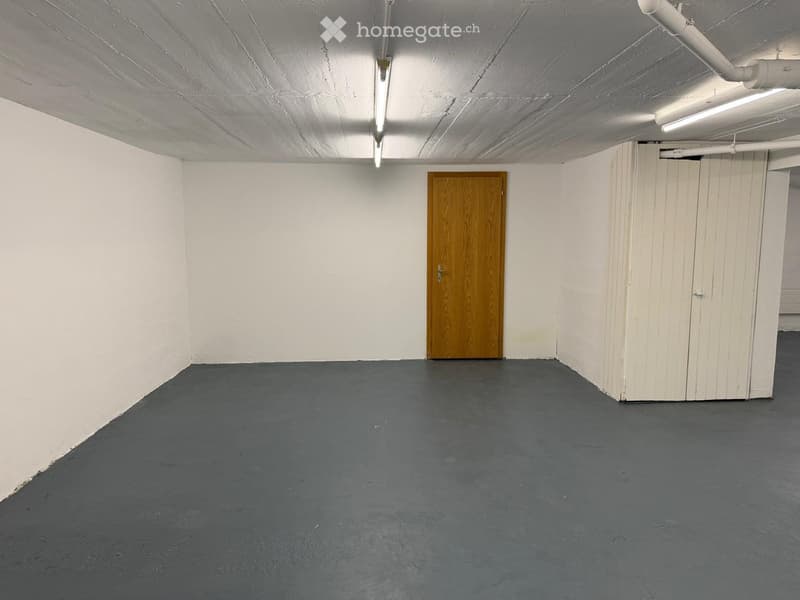 Empty room with white walls, grey floor, wooden door, and white cabinet.