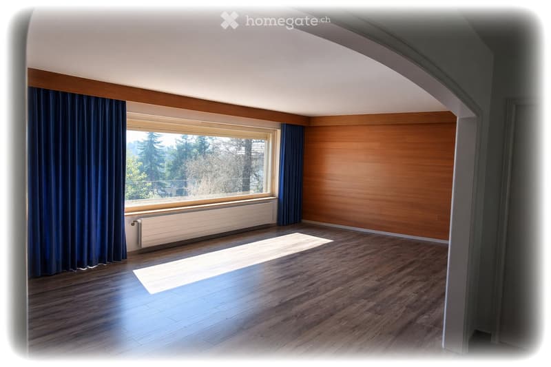 Empty room with wooden flooring, large window with blue curtains, radiator, and wooden panel wall.