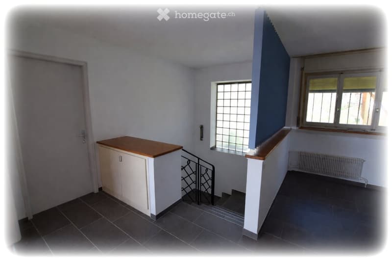 Empty room with tiled floor, white walls, a small cabinet, a staircase with a metal railing, and two windows with blinds.