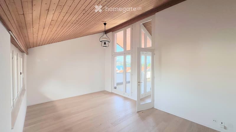 Empty room with white walls, wooden floor, large windows, and a hanging light fixture.