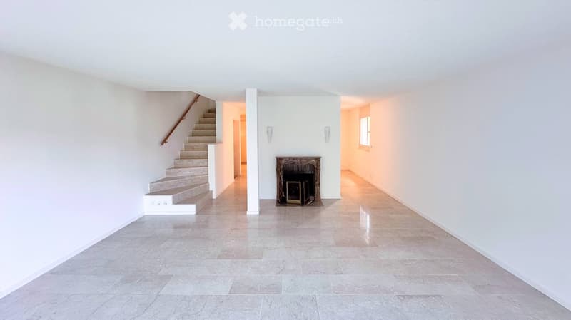Bright, open hallway with white walls, marble flooring, a staircase leading upwards, and a small fireplace in the center.