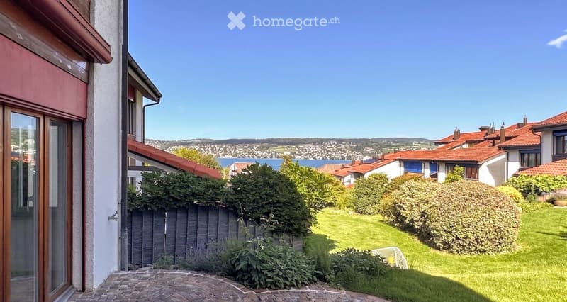 Well-maintained garden with green lawn, trimmed bushes, and a view of a coastal town and water in the background.