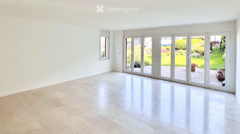 Empty room with white walls, large sliding glass doors leading to a garden, and a polished tile floor.