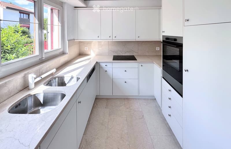 Modern kitchen with white cabinets, stainless steel sink, and built-in oven. Features marble countertops and tiled flooring.