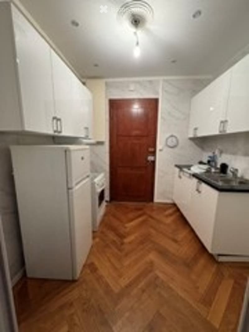 Bright kitchen with white cabinets, wooden herringbone flooring, refrigerator, oven, and sink.