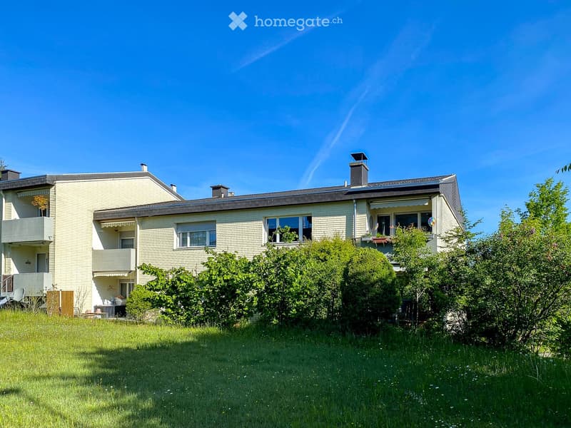 Two-story house with light yellow brick facade, multiple windows, balconies, and a well-maintained lawn.