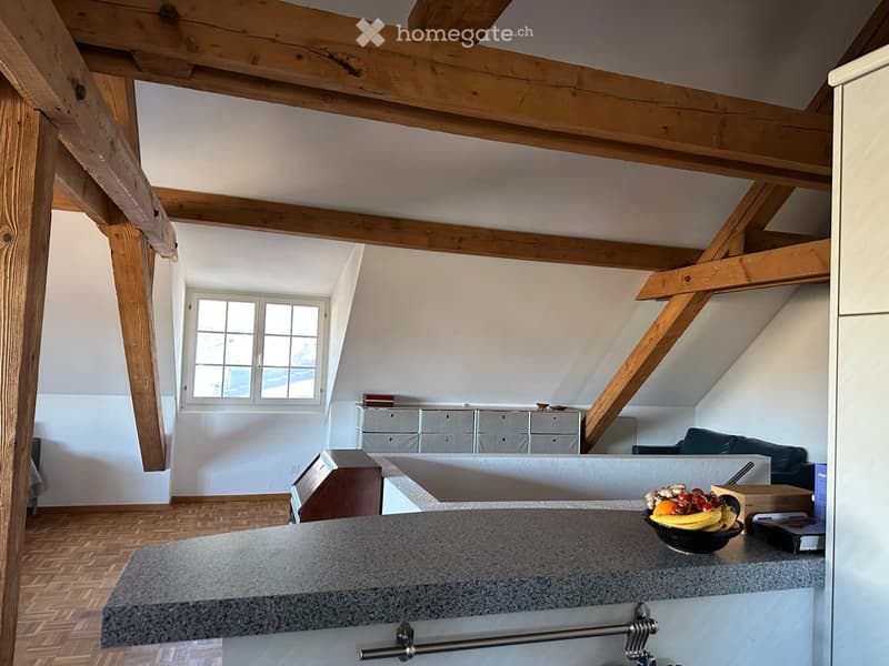 Loft-style room with exposed wooden beams, a grey countertop, a bowl of fruit, a sofa, and a grey cabinet with drawers.