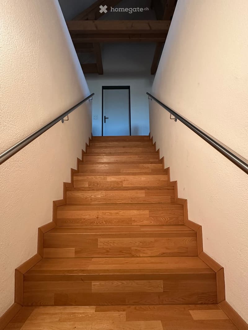 Wooden staircase with metal handrails, leading to a closed door at the end of the hallway.