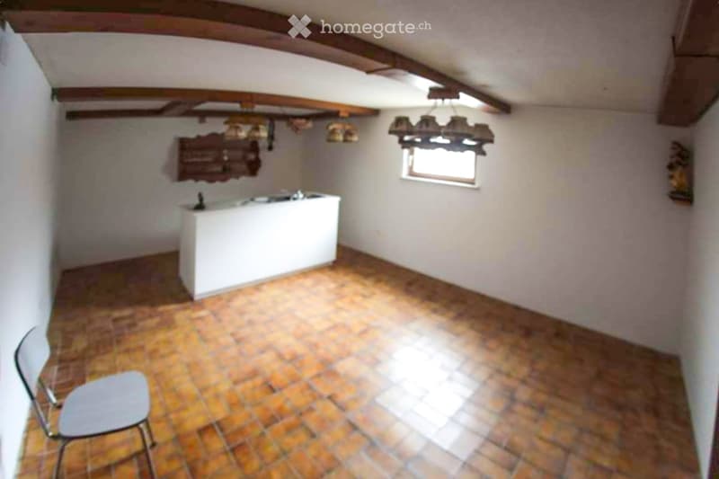A small, rustic room with exposed wooden beams, brick flooring, a white counter, and a single stool.