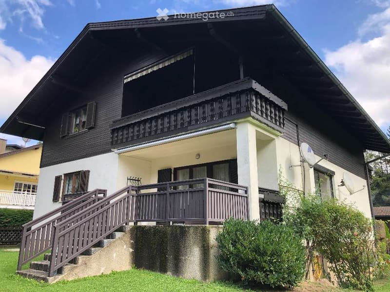 Two-story house with dark wooden exterior, white lower section, multiple balconies, and a staircase leading to the ground floor.