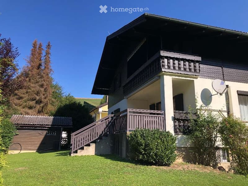 Two-story house with a balcony, wooden exterior, and a well-maintained lawn.