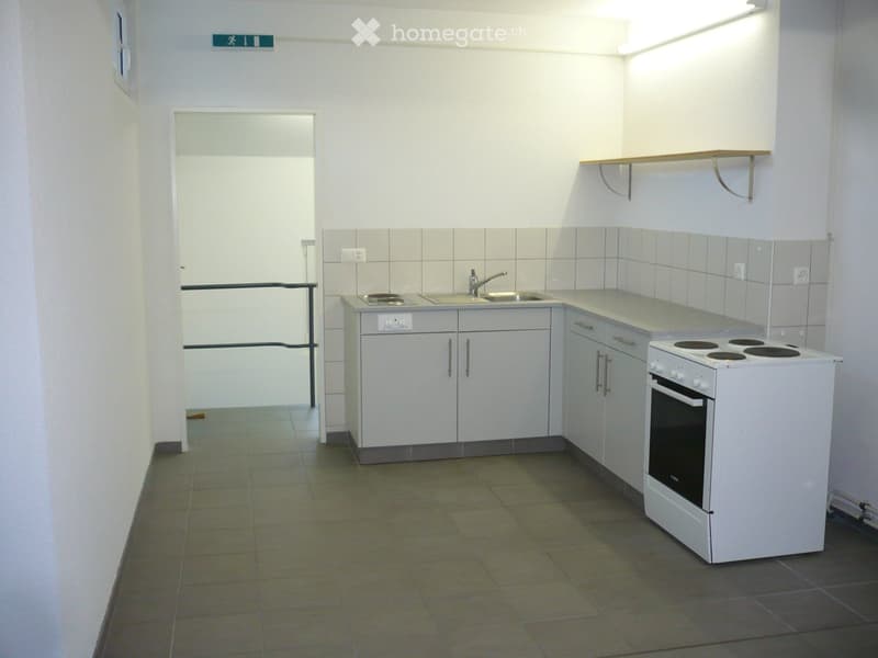 Modern kitchen with white cabinets, a sink, a stove, and an oven. The space is well-lit with tiled walls and a tiled floor.