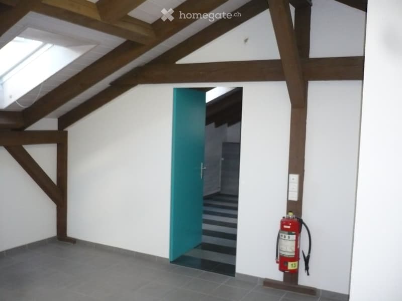Empty hallway with exposed wooden beams, a green door leading to a staircase, and a red fire extinguisher mounted on the wall.