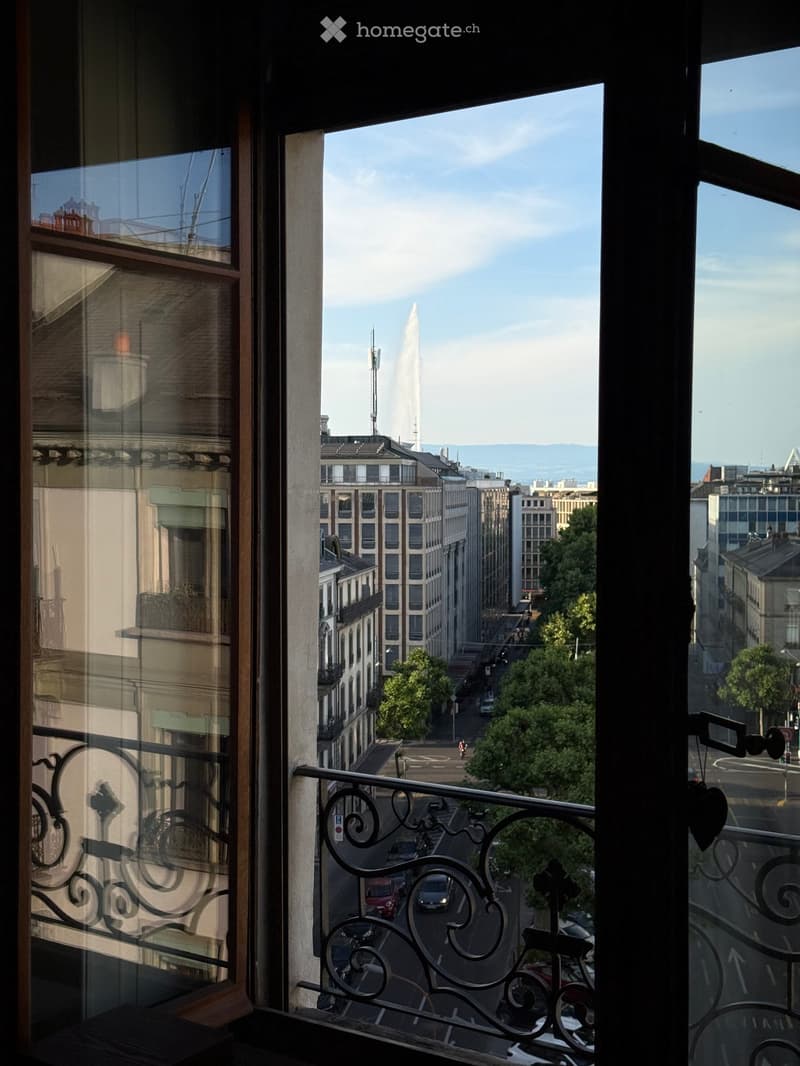 Balcony overlooking a cityscape with a prominent fountain in the distance, surrounded by buildings and trees.