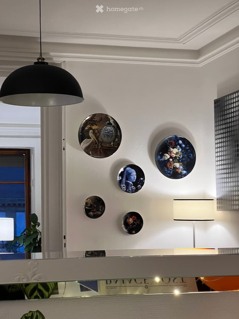 Elegant hallway with white walls, decorative plates, a black pendant light, and a glass railing with a plant visible in the background.