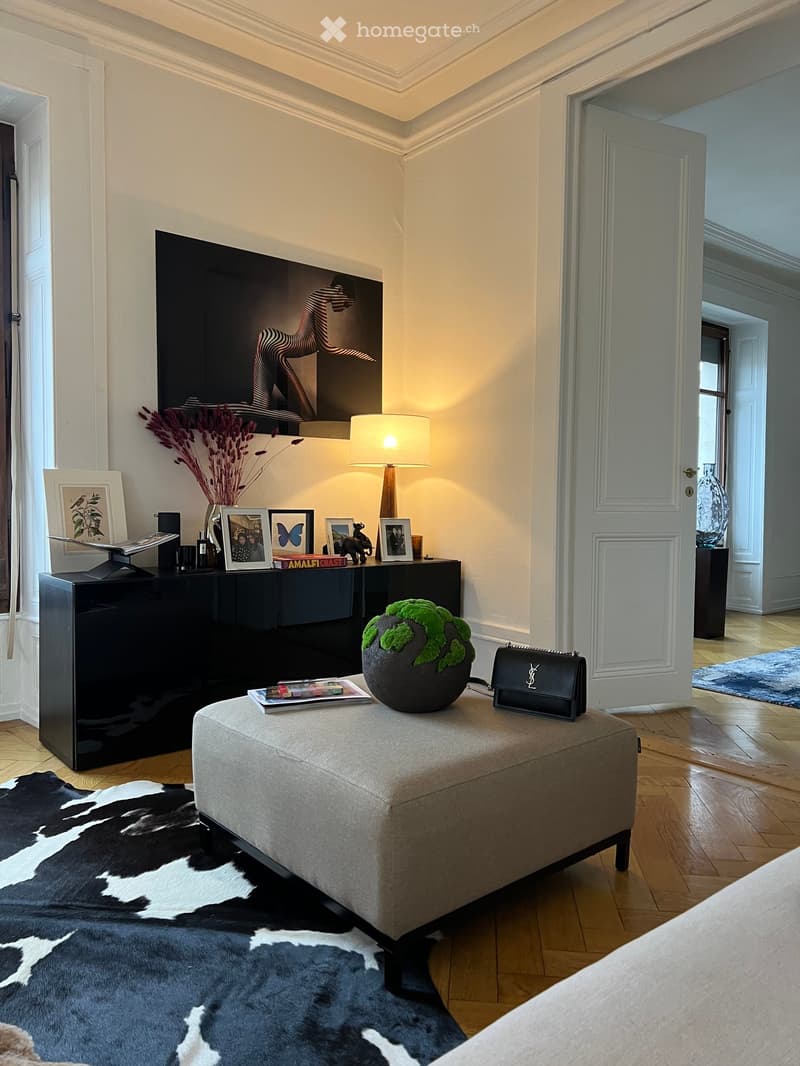 Elegant living room with a grey sofa, wooden floor, cowhide rug, side table with lamp, and decorative items including a mirror, picture frames, and a vase.