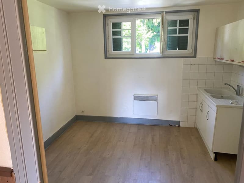 Empty room with wooden flooring, white tiled walls, a window, a radiator, and a small sink with cabinets.