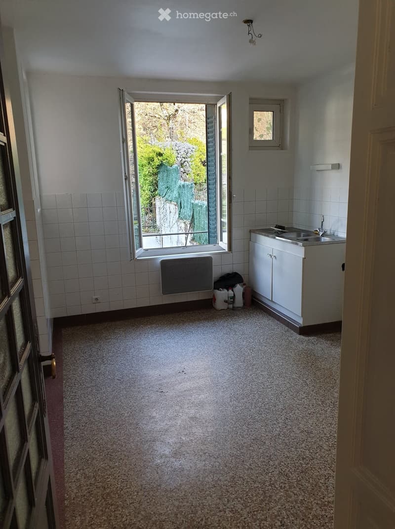 Empty room with tiled walls, carpeted floor, white cabinet, sink, and open window showing outdoor view.