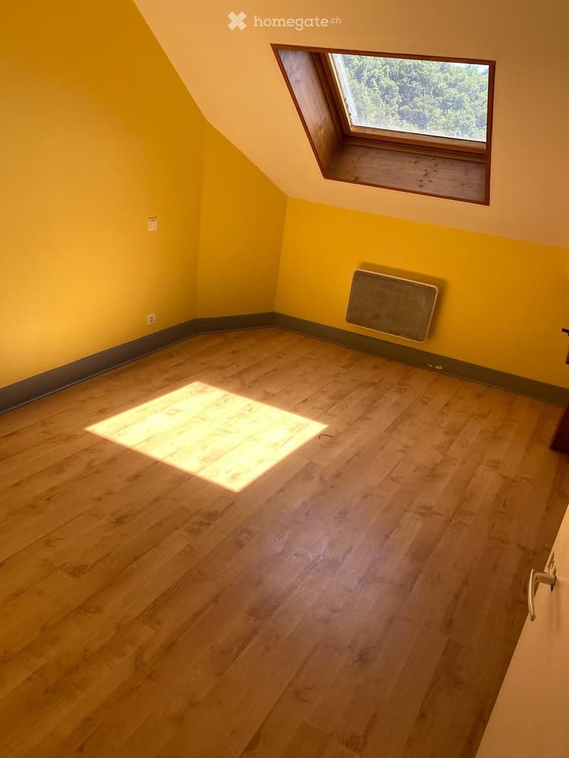 Bright, empty attic room with wooden flooring, yellow walls, and a skylight window allowing natural light to enter.