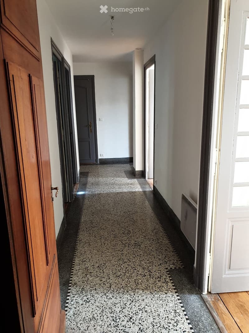 Long hallway with patterned tile floor, white walls, wooden doors, and a radiator on the right side.