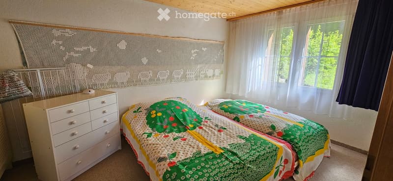 Cozy bedroom with a double bed covered in a green and yellow quilt, a white dresser with multiple drawers, and sheer white curtains on the windows.