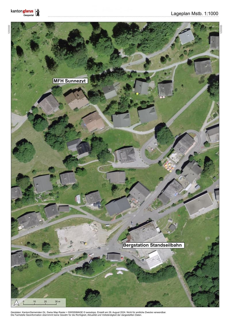 Aerial view of a residential area with multiple houses, roads, and green spaces. The area is labeled 'MFH Sunnezeit' and includes a marked location 'Bergstation Standseilbahn'.