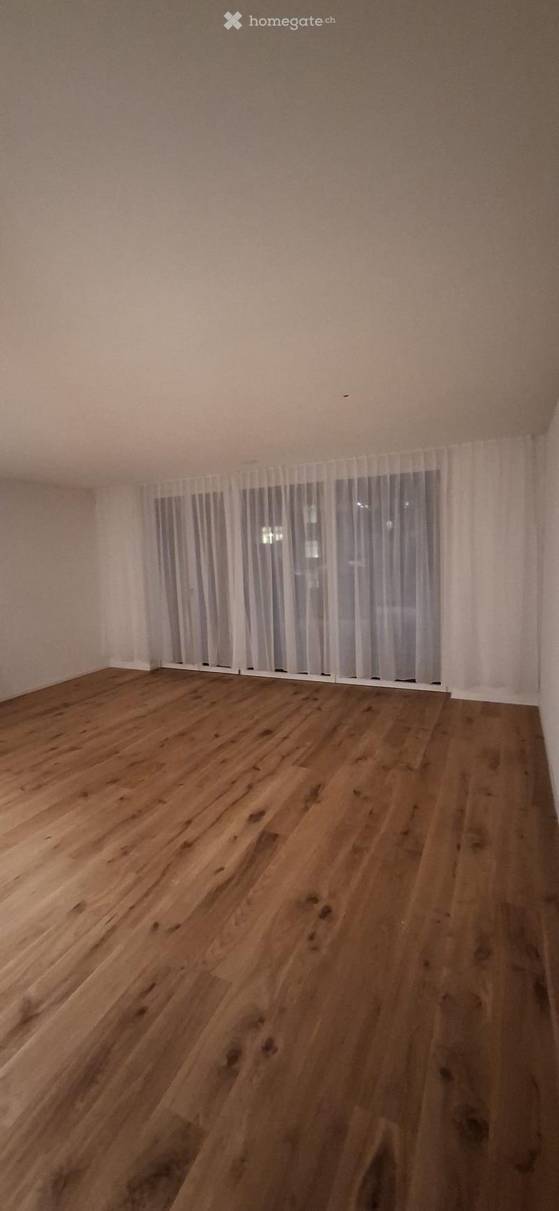 Empty room with hardwood floor, white walls, and white curtains.