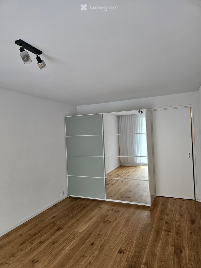 Unfurnished Room. Empty room with light grey walls, wooden flooring, and a large mirrored closet. A white door is visible on the right side.