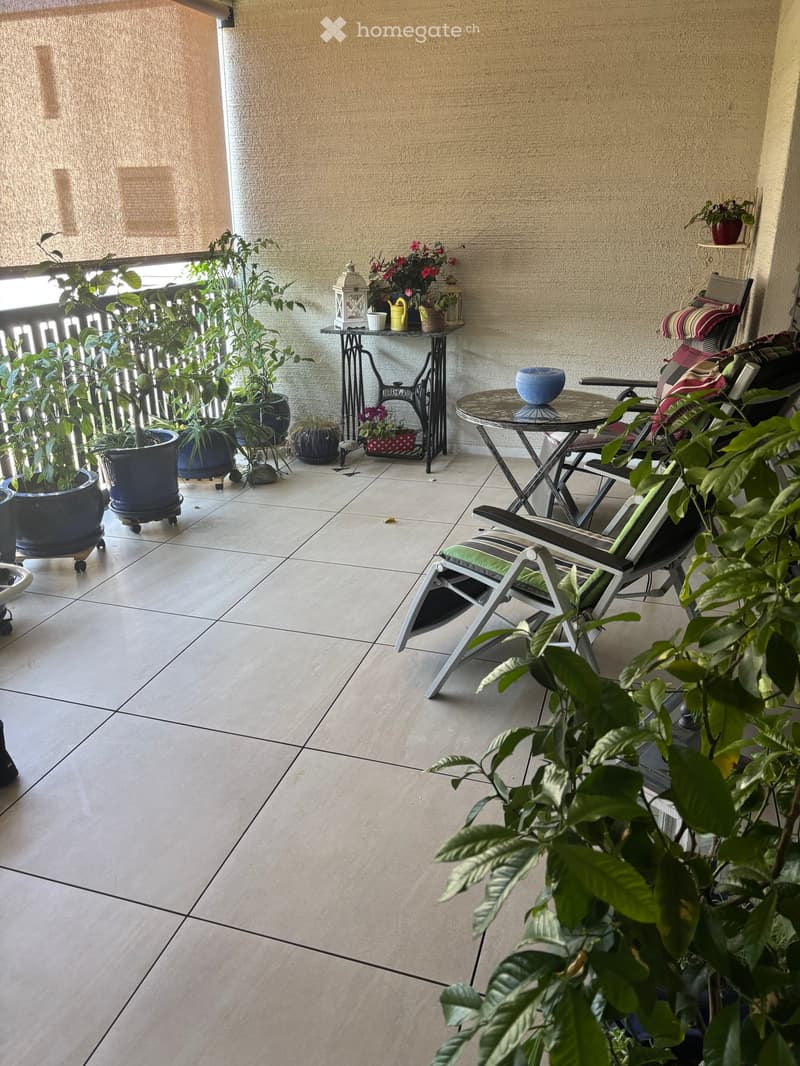 Balcony with tiled floor, small table, chairs, and several potted plants.
