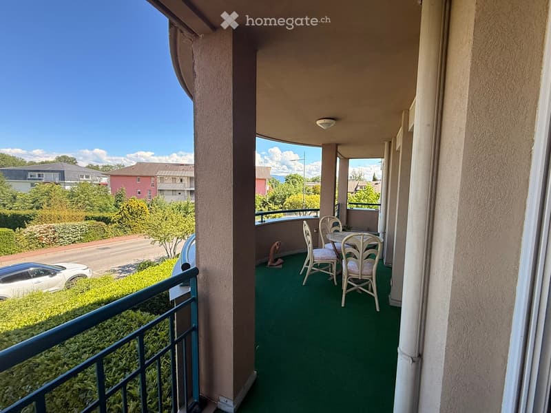 Balcony with green carpeting, white table and chairs, overlooking a street with houses and trees.