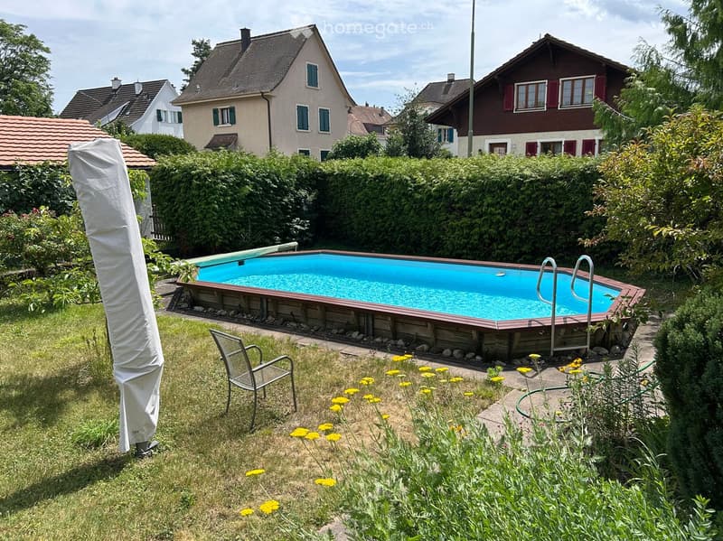 Private garden with a swimming pool, surrounded by greenery and yellow flowers, with a metal chair nearby.