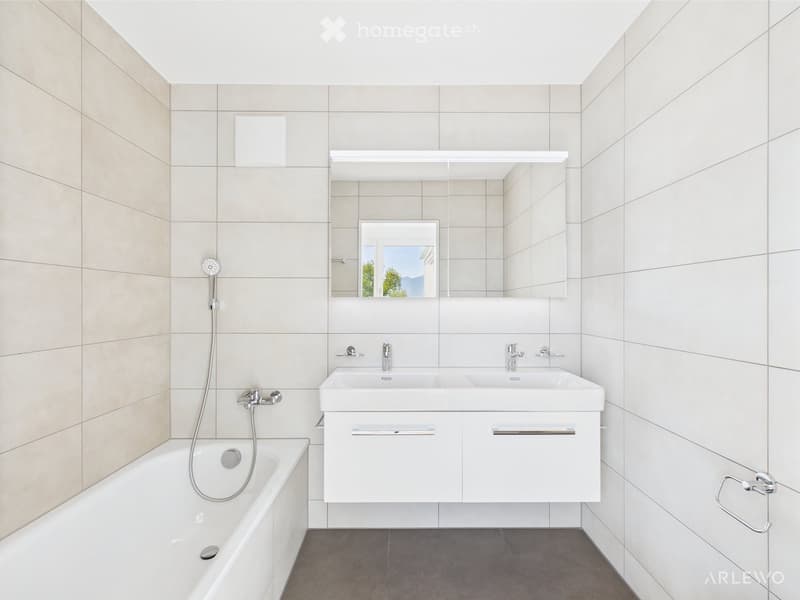 Modern bathroom with a white bathtub, double sink vanity, large mirror, and tiled walls.