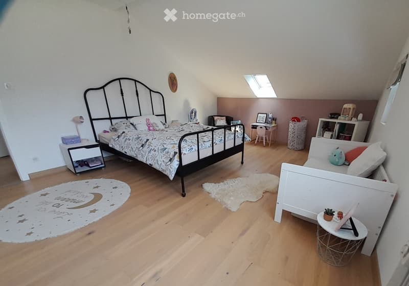 Cozy children's bedroom with wooden flooring, two beds, nightstands, a small table, and decorative rugs.