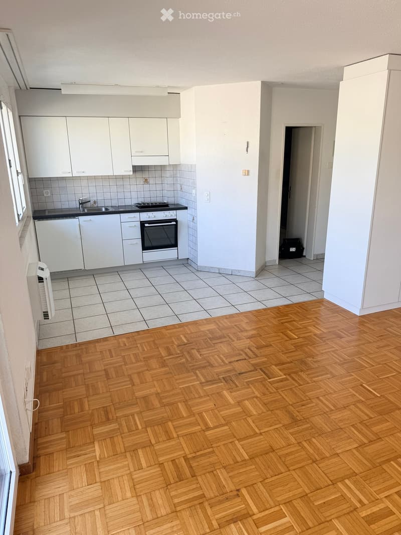 Empty room with wooden herringbone flooring, white cabinets, and a tiled kitchen area with sink, stove, and oven. No furniture or personal items present.