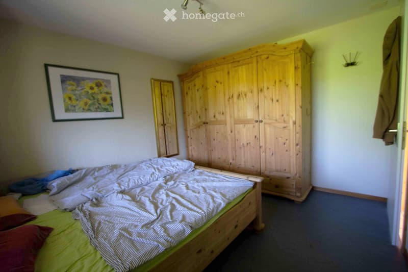 Bedroom with a wooden bed, green bedding, a large wooden wardrobe, and a picture frame on the wall.