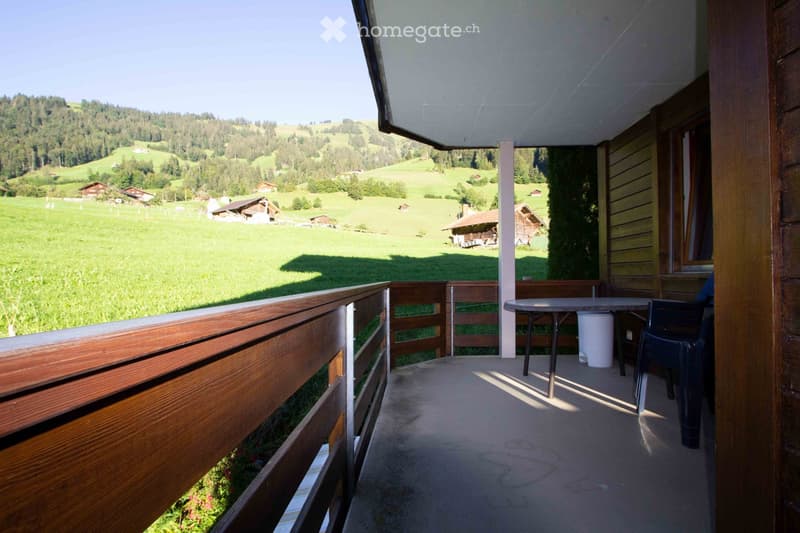 Balcony with wooden railing, overlooking a green valley with scattered houses and trees.