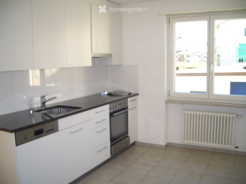 Modern kitchen with white cabinets, black countertop, sink, faucet, oven, and radiator under large windows.