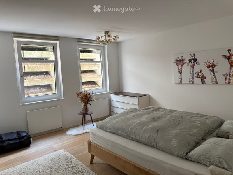 Bedroom with a wooden bed, nightstand, small stool, vase with dried flowers, radiator, and a colorful giraffe-themed picture on the wall.