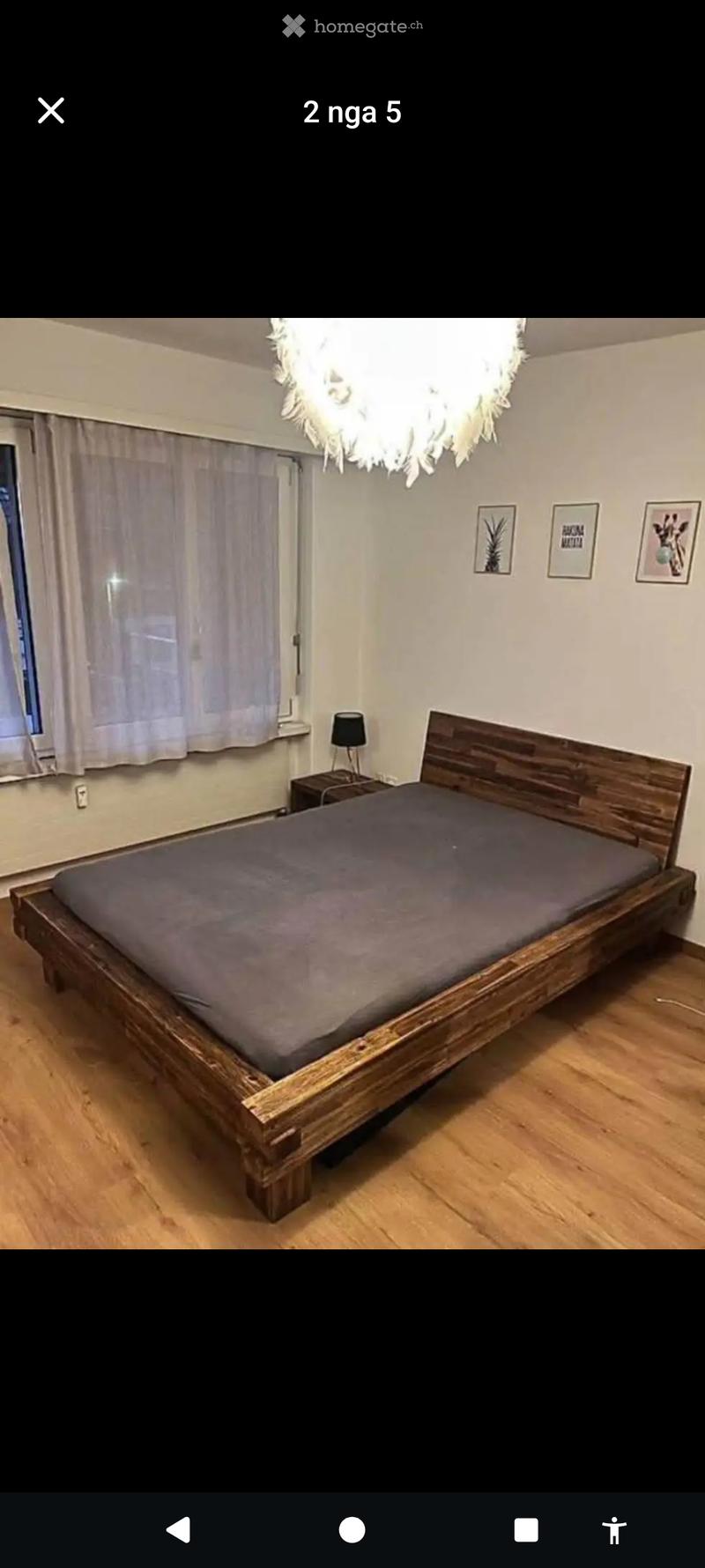 A modern bedroom with a wooden bed, dark grey bedding, a nightstand with a lamp, and several picture frames on the wall.