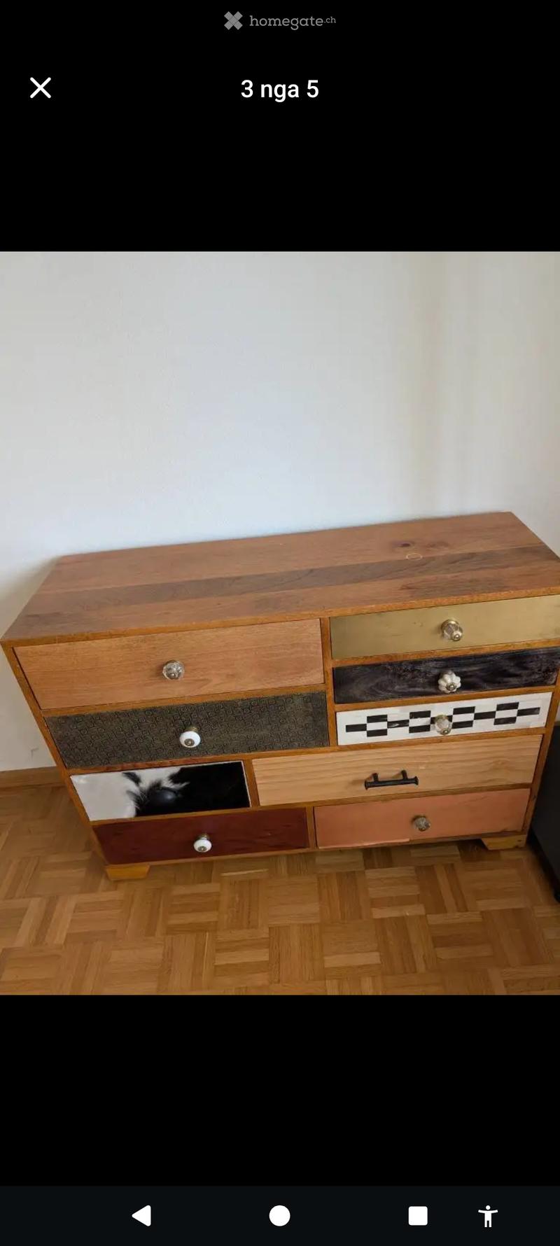 A wooden dresser with multiple drawers and various finishes, placed against a white wall on a wooden floor.