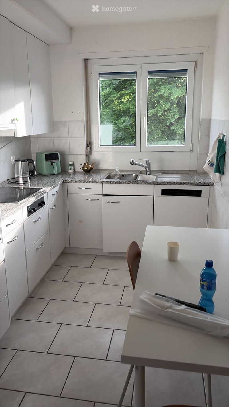 Modern kitchen with white cabinets, granite countertops, and stainless steel appliances. Features a sink, coffee maker, and a small dining area with a chair and table.