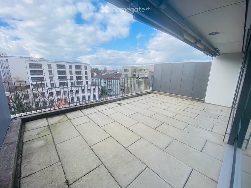Balcony with tiled floor, metal railing, and a view of surrounding buildings and a partly cloudy sky.