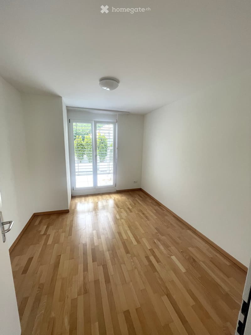 Empty room with wooden flooring, white walls, and a large sliding glass door leading to a balcony.
